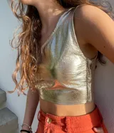 Top corto ajustado de cuero ovino color dorado metalizado, con escote asimétrico (un solo hombro) y cierre lateral.