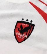 Camisa masculina de manga corta, color blanco con detalles en rojo en los hombros y mangas. Presenta el logo "MAVERICK" en el pecho izquierdo y un escudo con un ave y la palabra "OSAKA" en el pecho derecho.