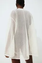 Túnica corta blanca de punto liviano con cuello corto y abertura en V adelante. Modelo de corte holgado con hombros caídos, mangas largas holgadas y bajo recto.