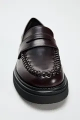Zapato plano tipo mocasín color borgoña de cuero charol, con detalle de pasados en la parte delantera, copete subido, antifaz y acabado en punta redondeada.