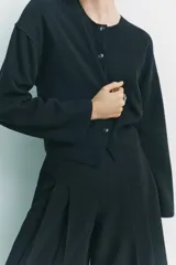Chaqueta color crema de punto canalé con cuello redondo, manga larga y cierre frontal con botones marrones.