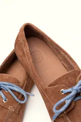 Mocasín tipo boat shoe con estampado de vaca en tonos marrón y blanco, confeccionado en cuero. Cuenta con cordones de cuero marrón oscuro y suela de goma.