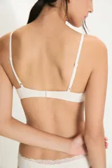 Conjunto de lencería de dos piezas color blanco roto, compuesto por un soutien sin aro con tirantes finos y un borde de encaje festoneado en el escote, y una bombacha tipo bikini con el mismo detalle de encaje en el borde superior.