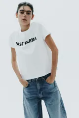Camiseta blanca de algodón con cuello redondo, manga corta y texto 'FAST KARMA' estampado en el frente.