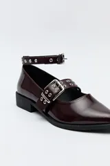 Zapato tipo zueco negro charol con punta fina, doble tira con hebillas metálicas y pulsera al tobillo con tachas.