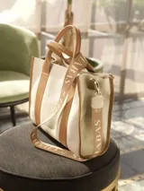 Bolso tote color crema con detalles en cuero marrón. Tiene doble asa de mano y correa de hombro extraíble con el logo de la marca.