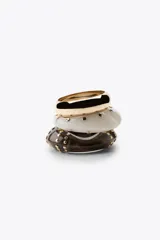 Set de tres pulseras rígidas: una dorada de metal y dos de resina, una color crema y otra marrón, ambas con tachas doradas.