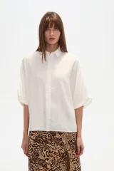 Camisa blanca de manga corta con cuello camisa y calce holgado. La tela presenta una textura arrugada o plisada sutil.