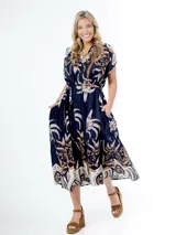 Vestido midi de algodón italiano, color azul marino con estampado en tonos blanco, beige y naranja/marrón. Presenta mangas cortas tipo murciélago, cuello en V con botones frontales y lazo desmontable para ajustar a la cintura.