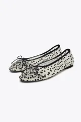 Zapato tipo bailarina de malla color blanco con estampado de lunares negros, detalle de lazo en la puntera, tirador trasero y suela plana.