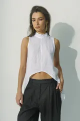 Top sin mangas blanco con cuello alto y bajo asimétrico, de textura arrugada.