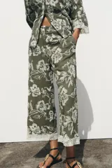Pantalón de tiro alto color verde oliva con bordado floral blanco, bolsillos laterales ocultos, pernera ancha y terminación en guipur.