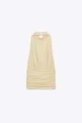 Top color crema con cuello halter, espalda descubierta, detalle de frunces y pieza metálica en forma de sol en el delantero.