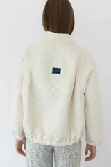 Campera acolchada color crudo con patrón de rombos, cuello alto y cierre frontal.