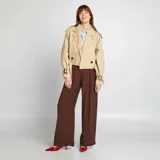 Gabardina corta color beige con cuello solapa, manga larga con trabillas ajustables, cierre cruzado con botón y cinturón.