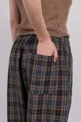 Pantalón largo de corte amplio con estampa escocesa en tonos grises, marrones y blancos. Tiene cintura elástica y tejido suave al tacto.