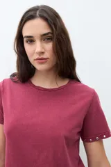 Remera de algodón color bordó, con cuello redondo, manga corta y detalle de ojalillos metálicos en el borde de las mangas.