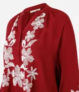 Blusa color borgoña de batista con cuello en V y botones. Presenta bordados florales blancos en el frente y las mangas largas con puños elásticos.