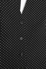 Chaleco negro con estampado de lunares blancos, escote en V, cuello halter con lazo y cierre frontal con botones.