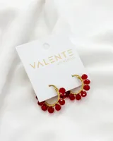 Aros de acero dorados, tipo argolla, con cuentas de cristal rojas colgando.