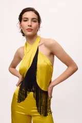 Top amarillo de satén con cuello halter y flecos negros.