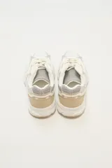 Zapatillas deportivas blancas con detalles en plateado y beige, con cordones y suela gruesa.