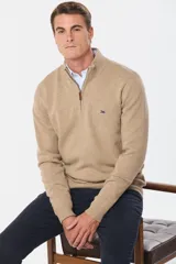 Buzo tejido de lana color beige, con medio cierre metálico y cuello alto. Tiene un pequeño logo bordado en el pecho.