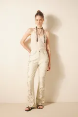 Pantalón de cuero ovino color crema con bordado de tachas metálicas y piedras en frente y espalda. De corte jeanero con calce flare, acceso delantero con botón metálico y cierre, bolsillos delanteros y traseros.