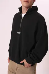 Sudadera negra con cierre de cremallera metálica en el cuello y estampado con texto en el pecho.