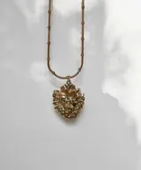 Collar plateado con cadena de eslabones y dije en forma de corazón con detalles ornamentales y una piedra en el centro.