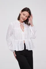 Blusa blanca con rayas verticales, cuello con lazo, mangas largas y corte holgado.