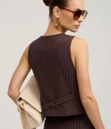 Chaleco entallado de mujer, color marrón oscuro con finas rayas verticales blancas (rayas de giz). Presenta escote en V, cierre frontal con botones forrados y bolsillos falsos.