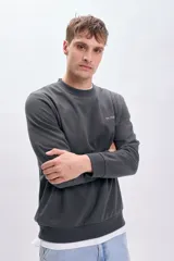 Sudadera gris oscuro de corte clásico con cuello redondo y puños y bajo acanalados. Presenta un pequeño bordado con letras en el pecho.