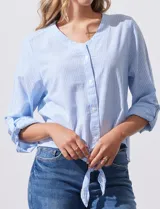 Blusa de algodón a rayas verticales finas en tonos blanco y lila, con escote en V, abertura frontal con botones y mangas largas regulables con presilla y botón. El ruedo termina anudado al frente.
