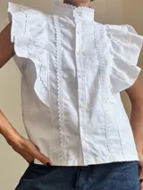 Camisa blanca sin mangas con detalles de encaje y volantes en los hombros.