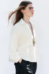Camisa color crudo confeccionada con lino, de corte recto, cuello solapa con escote pico y manga larga. Presenta aplicación de pasamanería en el frente y cierre frontal con botones forrados a tono.