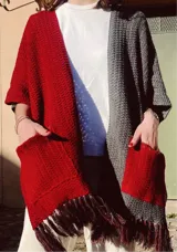 Ruana tejida con diseño color block, mitad roja y mitad gris, con mangas cortas y bolsillos frontales.