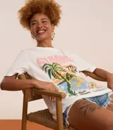 Remera de algodón color blanco, de corte alargado, con cuello redondo y manga corta. Presenta una estampa frontal de estilo tropical con palmeras, flores y texto 'Summer Tropical Beach'.