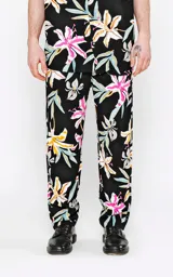 Pantalón recto unisex con estampado floral en tonos rosa, amarillo, celeste y blanco sobre fondo negro. Confeccionado en rayón.