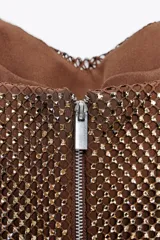 Top strapless color marrón, confeccionado en tejido tipo red con aplicación de strass y forro interior combinado. Presenta tejido drapeado y cierre en espalda con cremallera metálica.