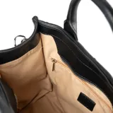 Cartera negra de tamaño mediano, confeccionada en símil cuero soft con diseño acolchado. Tiene doble asa de mano y correa bandolera regulable y extraíble. El acceso es con cierre y cuenta con un compartimento principal con bolsillos internos.