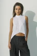 Top sin mangas blanco con cuello alto y bajo asimétrico, de textura arrugada.