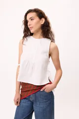 Musculosa blanca de algodón y lino, con tablas verticales en el frente y lazos laterales para regular el ajuste.