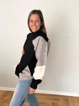 Suéter tejido con diseño geométrico en bloques de color negro, gris, blanco y terracota. Tiene cuello alto tipo polera y corte relajado.