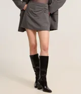 Short pollera corto color gris, de sastrería con cierre por cremallera invisible en la parte de atrás, pences y detalle en fruncido en el lateral.