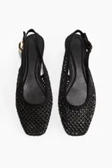 Sandalias bajas negras con capellada de malla tejida, punta fina y tira trasera con hebilla dorada.