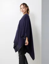 Ruana blanca de tejido suave, con ribete de eco cuero negro en los bordes y cierre frontal con botones metálicos dorados.