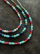 Gargantilla corta con cuentas de colores rojo, azul, blanco y beige con manchas negras. Se cierra con cadena de acero quirúrgico y ganchito para regular el largo.
