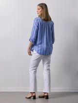 Camisa color beige con rayas verticales blancas, de lino, con cuello con solapa y abertura central con botones. Tiene un bolsillo aplicado en el pecho y mangas largas regulables con presilla y botón.