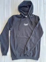 Buzo canguro negro con capucha y cordones ajustables. Estampado en la espalda con un diseño circular de una ola, un sol y una palmera.